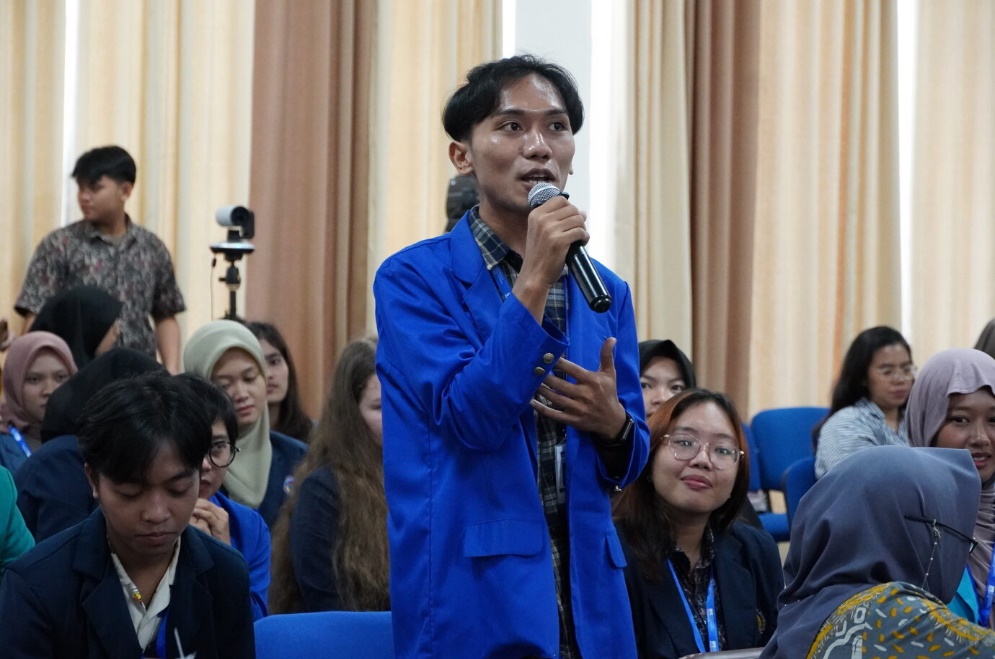 A person in a blue jacket speaking into a microphone
Description automatically generated