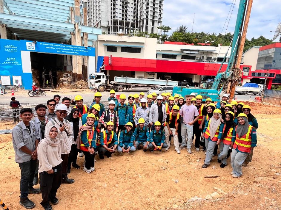 A group of people wearing hard hats and standing in front of a construction site Description automatically generated