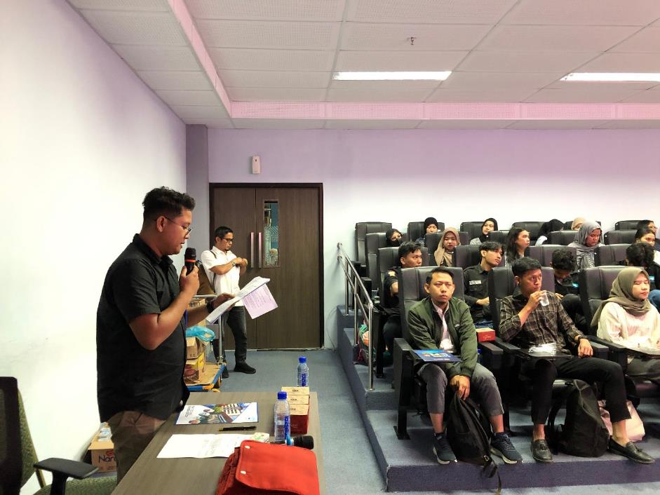 A person standing in front of a group of people in a room

Description automatically generated