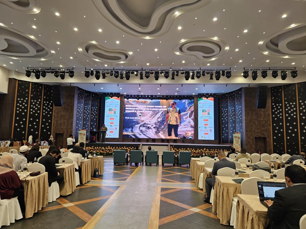 A room with people sitting at tables and a large screen

Description automatically generated