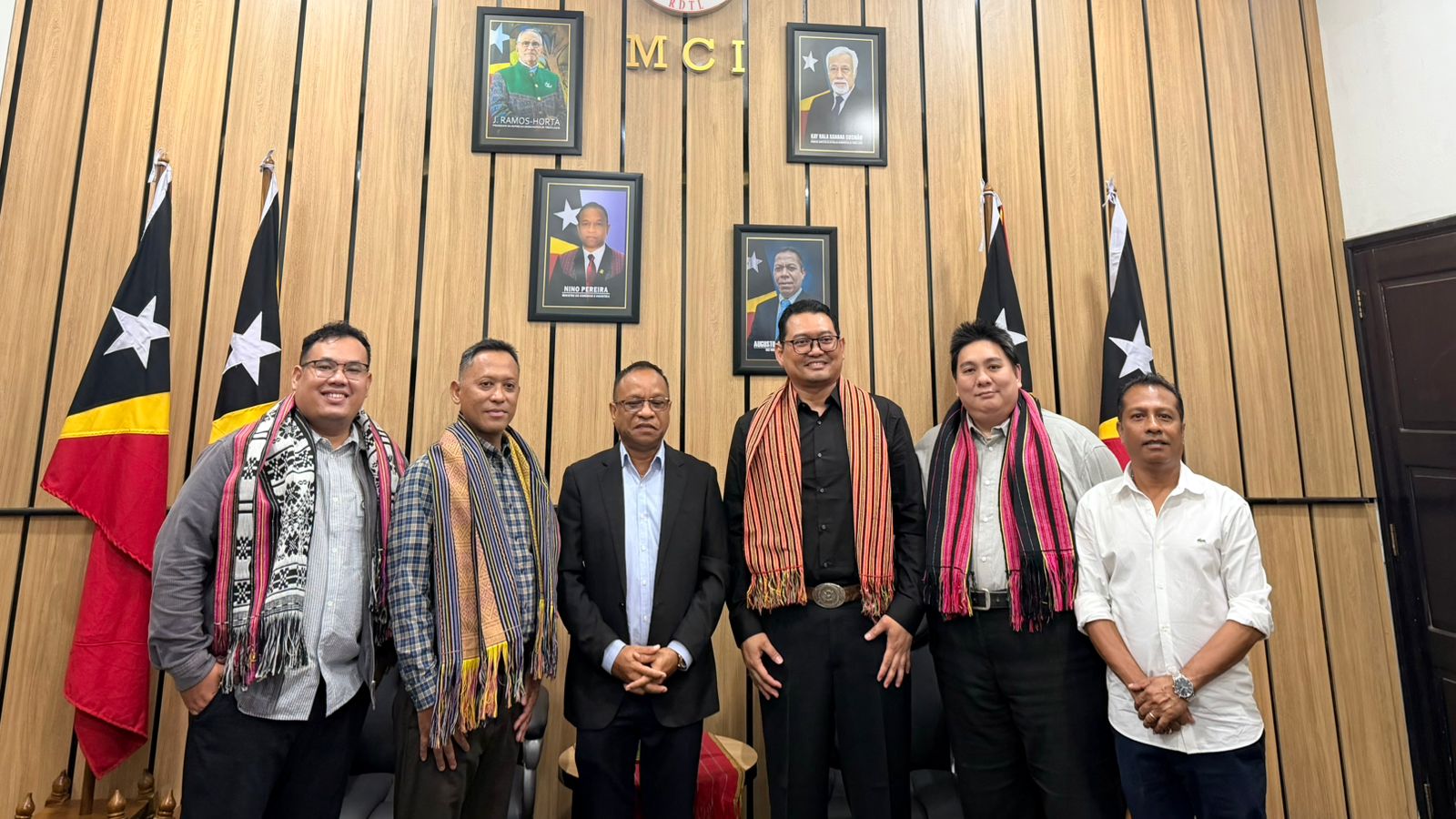 A group of men standing in front of a wall with flags
Description automatically generated