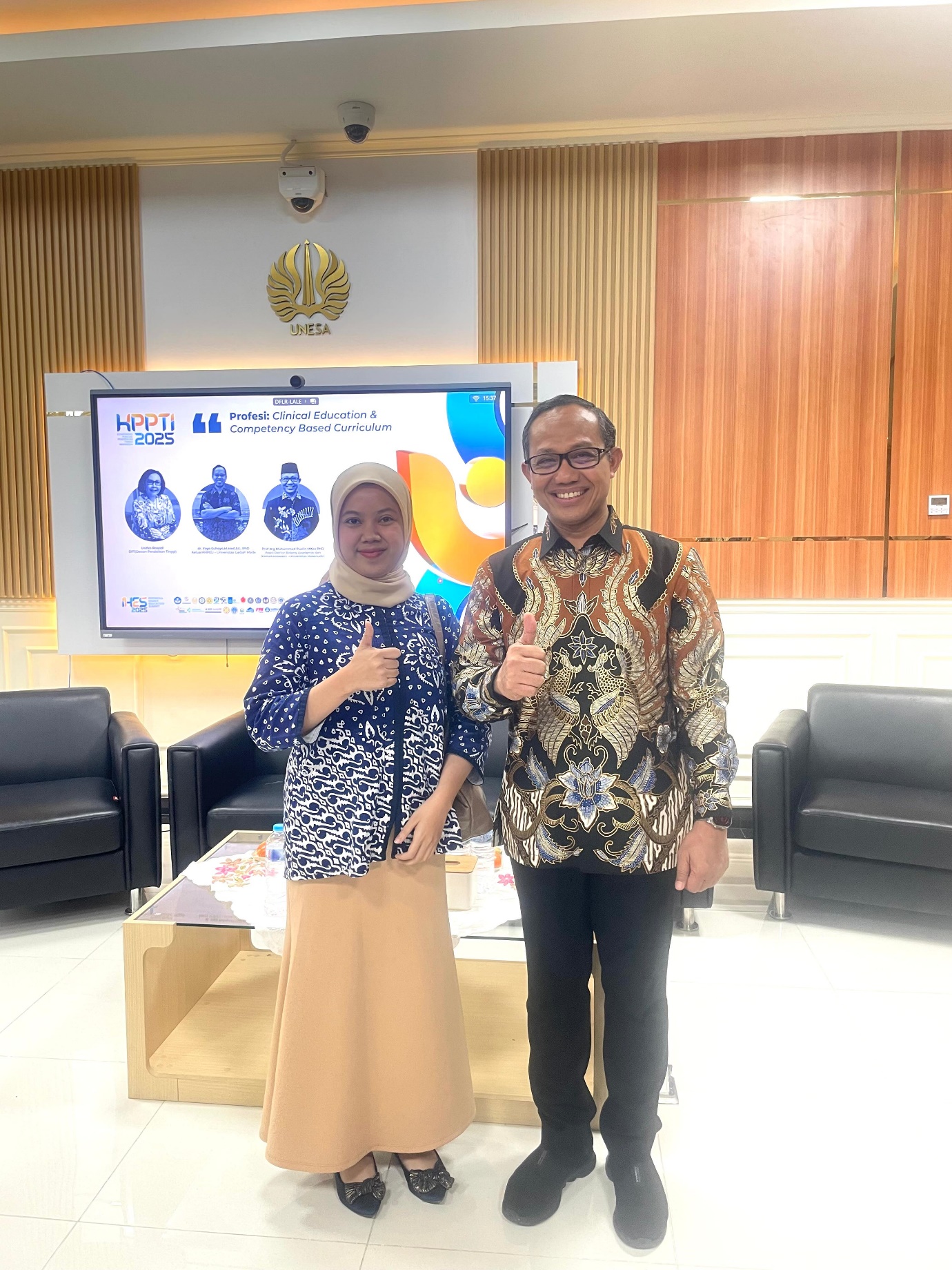 A person and person standing in a room with a large screen Description automatically generated