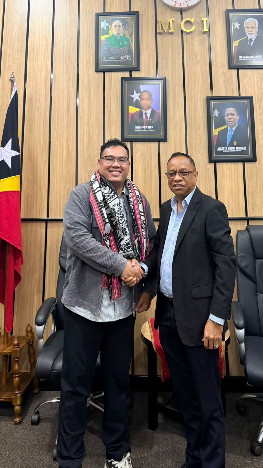 Two men shaking hands in a room
Description automatically generated