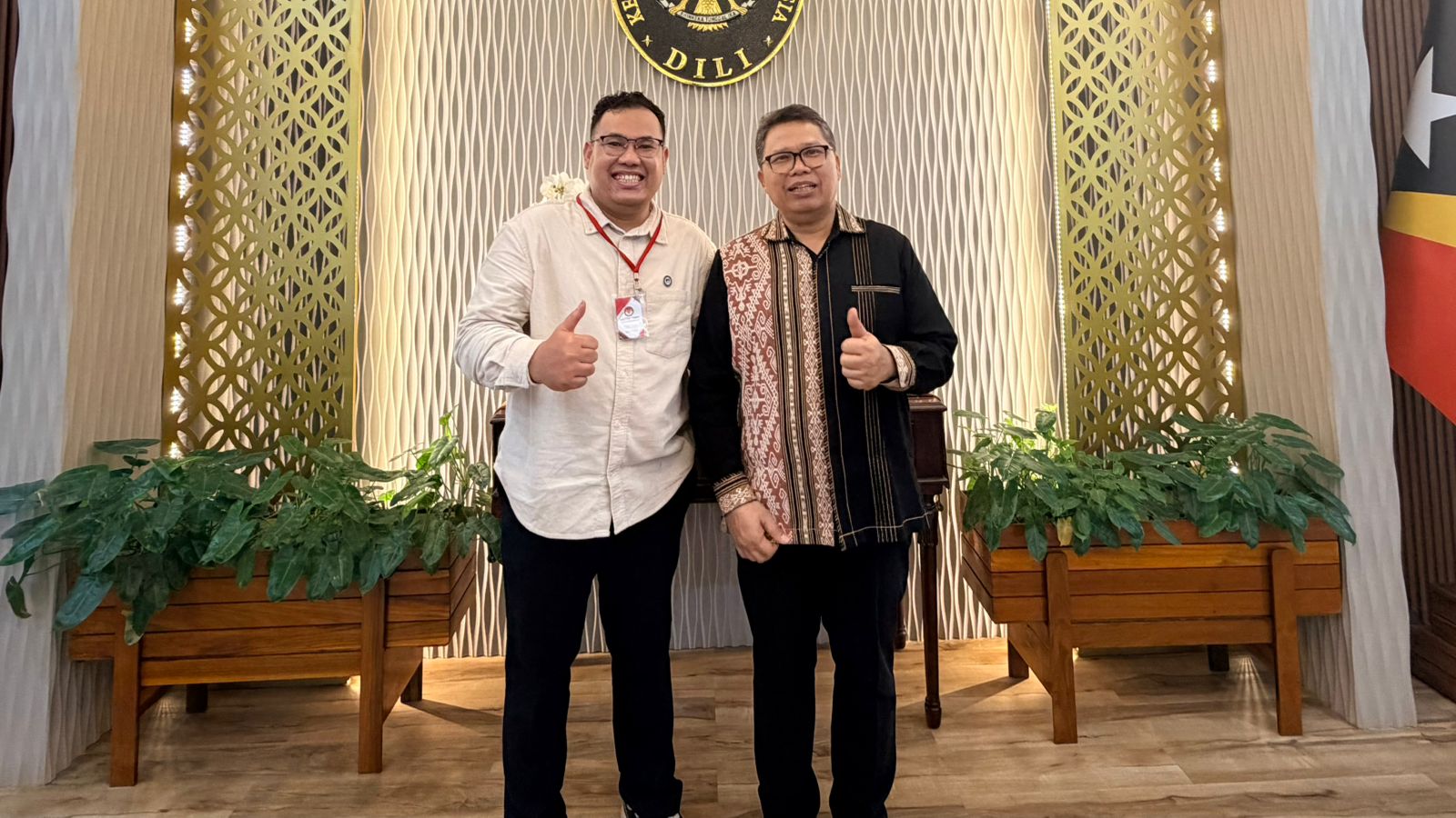 Two men standing in front of a wall with plants Description automatically generated